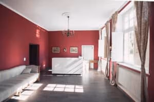 Firmeneventlocation 23 Raum mit roten Wänden, großen Fenstern, gestreiftem Sofa, Kronleuchter und weißem Empfangstresen – ideal für Hochzeiten oder Firmenevents.