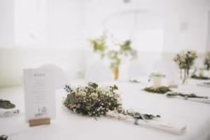 Wei&szlig; gedeckter Tisch mit Men&uuml;, Blumenschmuck und schlichtem Gr&uuml;n in der Eventlocation M&uuml;nster.