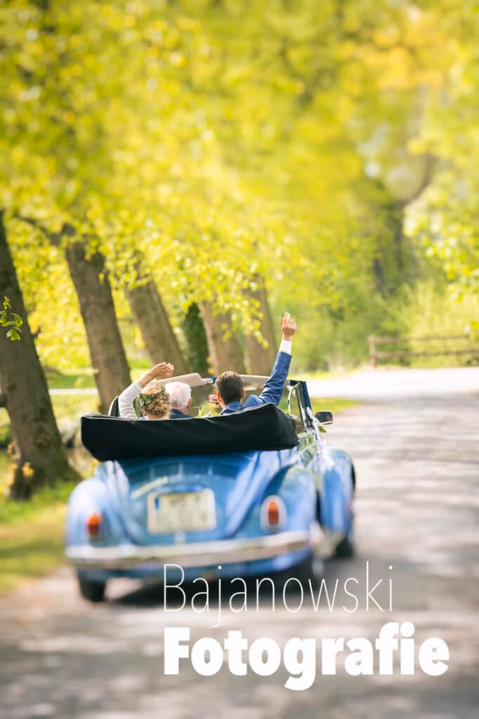 Ein Paar in einem blauen Cabrio genießt die Umgebung von Münster, perfekt für Firmenveranstaltungen. Text von Bajanowski Fotografie überlagert das Bild.