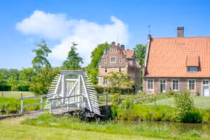 Firmeneventlocation 18 Eine kleine weiße Brücke überquert einen Bach in der Nähe zweier Backsteinhäuser – ideal für Firmenevents in Münster.